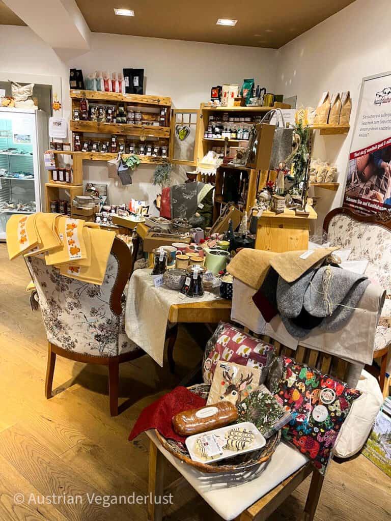 Dieses Bild zeigt eine gemütliche Ladenecke, die mit handgefertigten Waren, Gourmetprodukten und rustikaler Dekoration gefüllt ist. In den Regalen finden sich Marmeladen, Tees und handwerkliche Leckereien, während auf Tischen und Stühlen festliche Textilien, Geschenkartikel und verpackte Köstlichkeiten ausgestellt sind. Perfekt, um die einzigartigen und nachhaltigen Angebote einer lokalen Boutique zu bewerben. Sag mir Bescheid, wenn du einen SEO-freundlichen Alt-Text möchtest!
