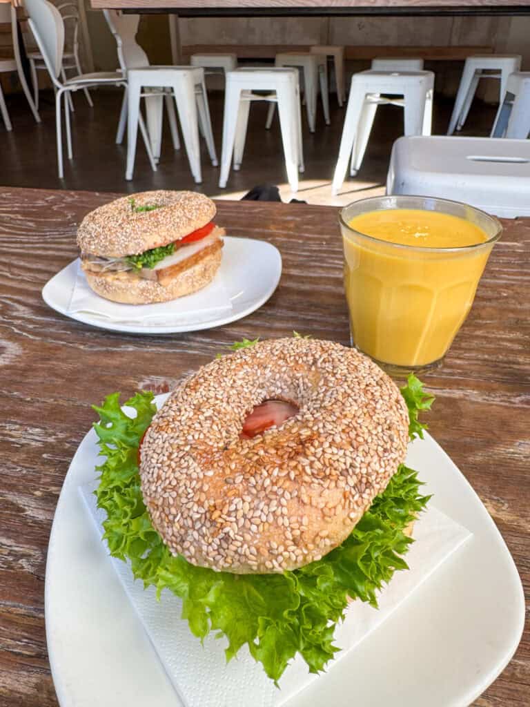 Zwei Sesambrötchen mit Füllungen auf Tellern, daneben ein Glas Mango Lassi.