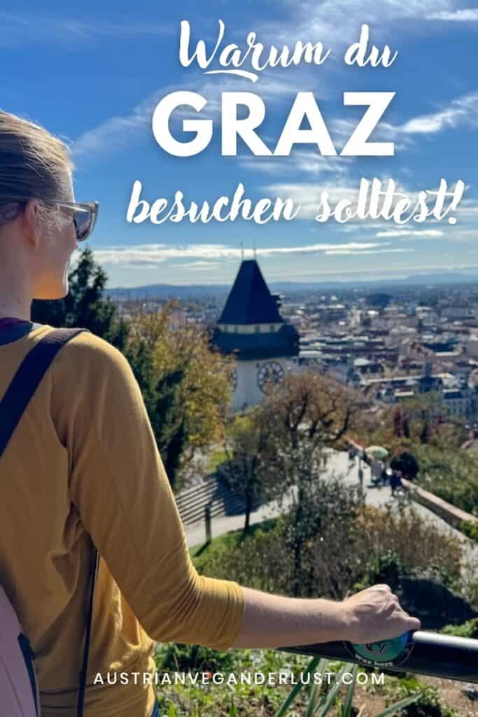 Eine Frau mit gelbem Oberteil und Rucksack schaut vom Schlossberg in Graz auf die Stadt hinab, mit dem berühmten Uhrturm im Vordergrund und einer klaren, sonnigen Aussicht. Text-Overlay: 'Warum du Graz besuchen solltest!' sowie die Website 'AustrianVeganderlust.com'.