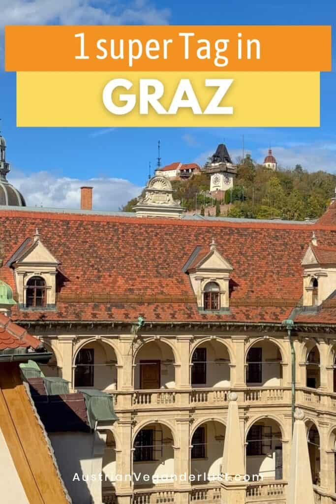 "Ein Bild mit der Aufschrift '1 super Tag in Graz' in orange und gelber Schrift auf einem blauen Himmelshintergrund. Im Vordergrund die roten Dächer und die historische Architektur des Grazer Landhauses, im Hintergrund der Schlossberg mit dem Uhrturm, umgeben von herbstlichem Grün. URL: AustrianVeganDerLust.com."