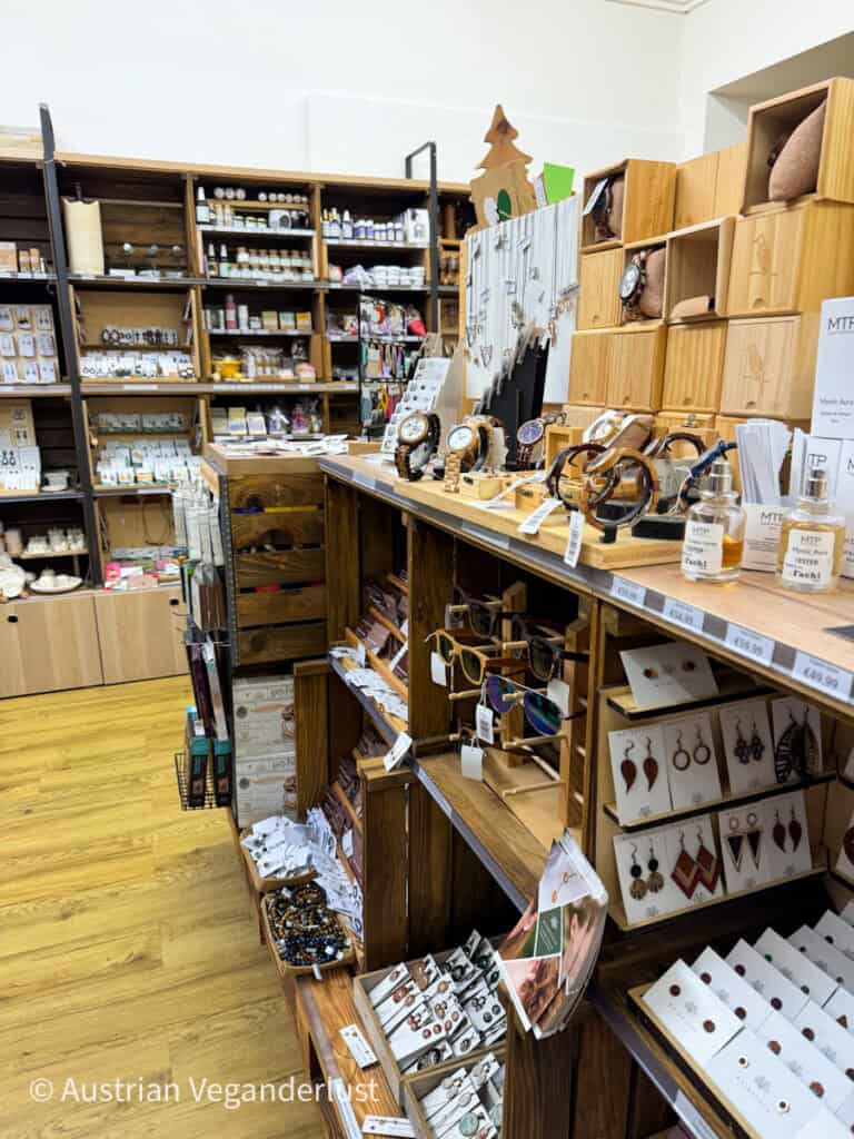 A boutique shop in Graz showcasing handmade and artisan goods displayed on wooden shelves and tables. Items include wooden watches, jewelry, sunglasses, essential oils, and decorative pieces, creating a cozy and natural aesthetic. The neatly arranged products and warm wooden tones invite browsing and highlight the artisanal craftsmanship.