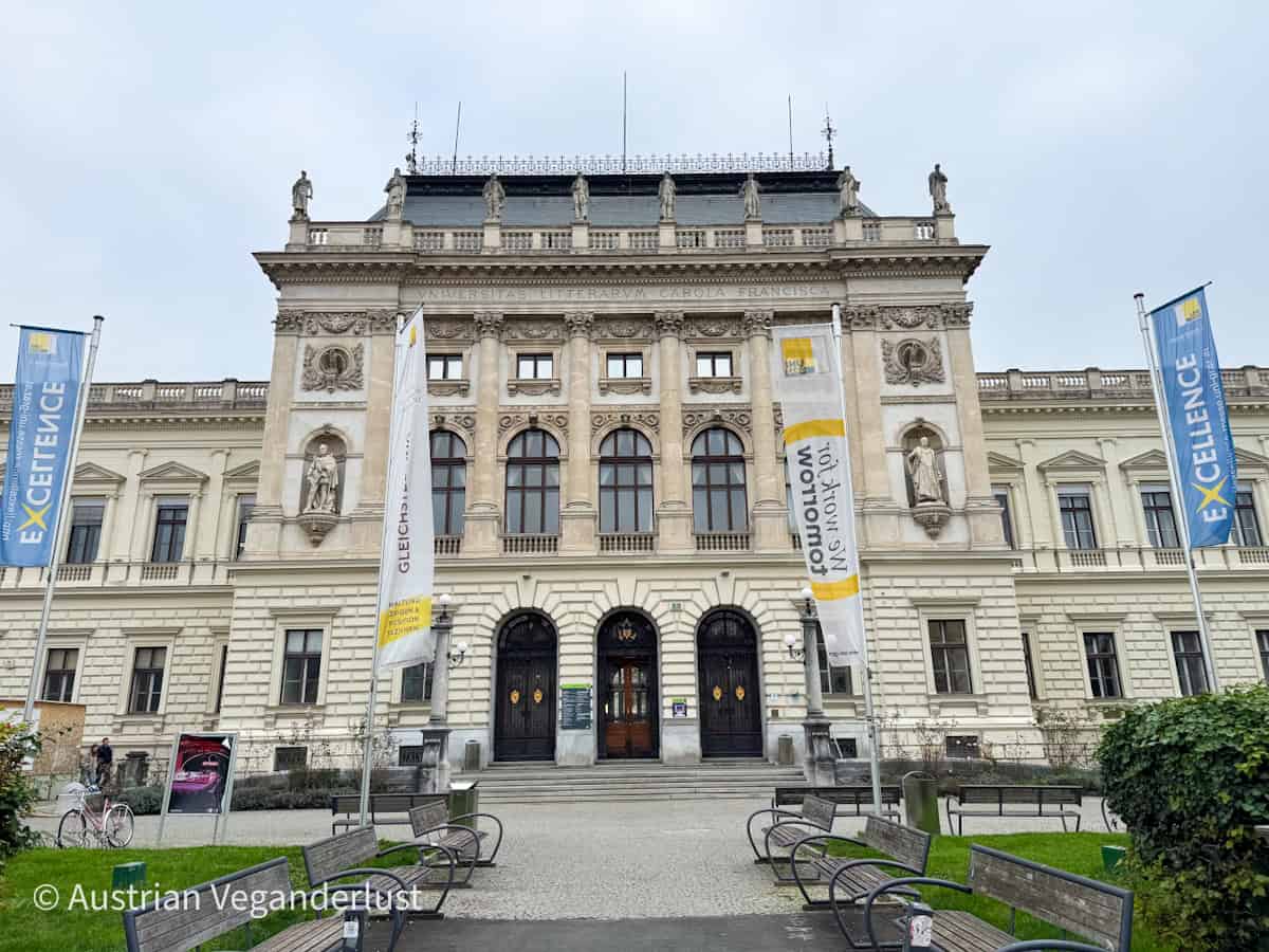 Die prächtige Fassade der Universität Graz, die eine beeindruckende Architektur mit Statuen und detaillierten Schnitzereien zeigt. Die Erkundung historischer Wahrzeichen wie der Universität bietet eine ungewöhnliche kulturelle Erfahrung für alle, die sich für das akademische und architektonische Erbe von Graz interessieren.