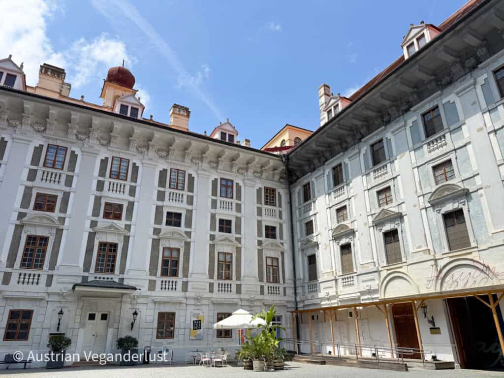 Heller Innenhof des Schlosses Esterházy in Eisenstadt mit weißen historischen Fassaden, hohen Fenstern, roten Ziegeldächern und einem kleinen Cafébereich im Freien.