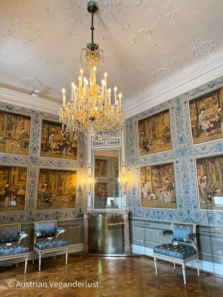 Luxuriöser Innenraum im Schloss Esterházy mit detaillierten Wandmalereien, blauen und goldenen antiken Stühlen, einem großen Kristallkronleuchter und einem reich gemusterten Holzboden.