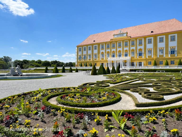 Weitläufige Frontansicht von Schloss Hof, mit einem gepflegten Garten im Vordergrund und leuchtend gelber und weißer Barockarchitektur.