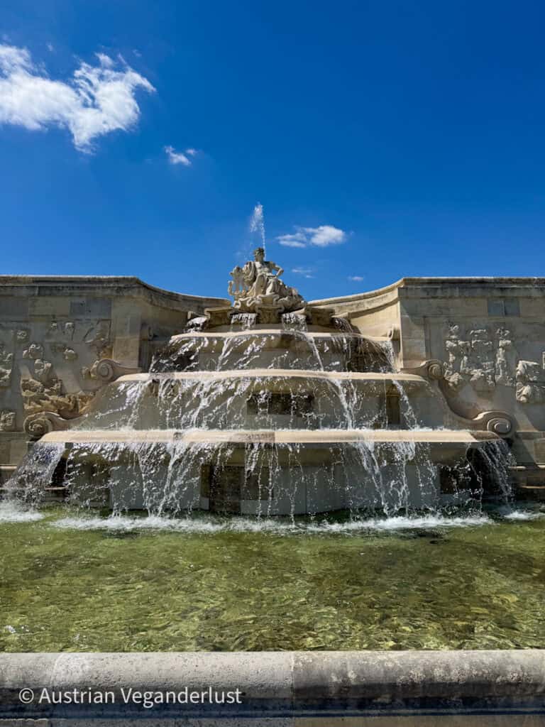 Tiered baroque fountain at Schloss Hof with cascading water and a sculpted central figure, set against a bright blue sky.