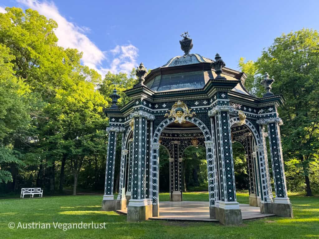 Verschnörkelter schwarz-weißer Dianatempel im Park von Schloss Laxenburg, umgeben von üppigen grünen Bäumen und einem grasbewachsenen Rasen.