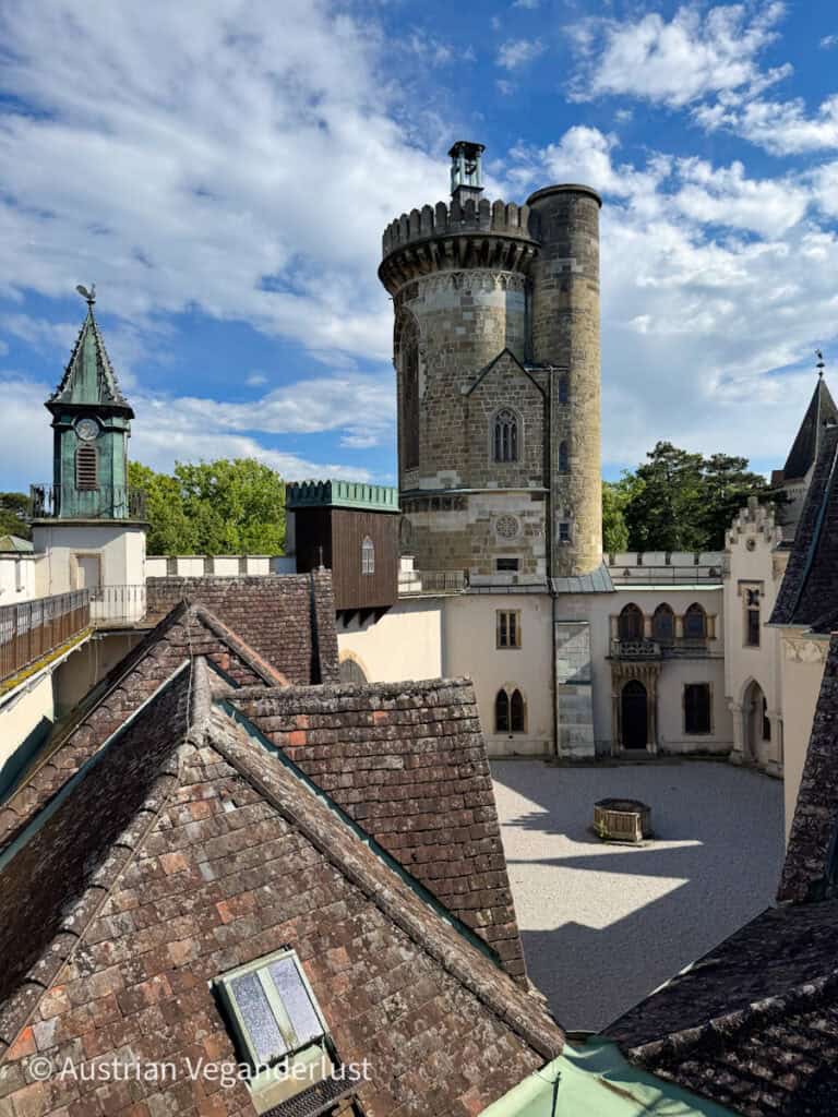 Blick über die Ziegeldächer auf den hohen, runden Turm der Franzensburg auf Schloss Laxenburg, bei teilweise bewölktem Himmel.