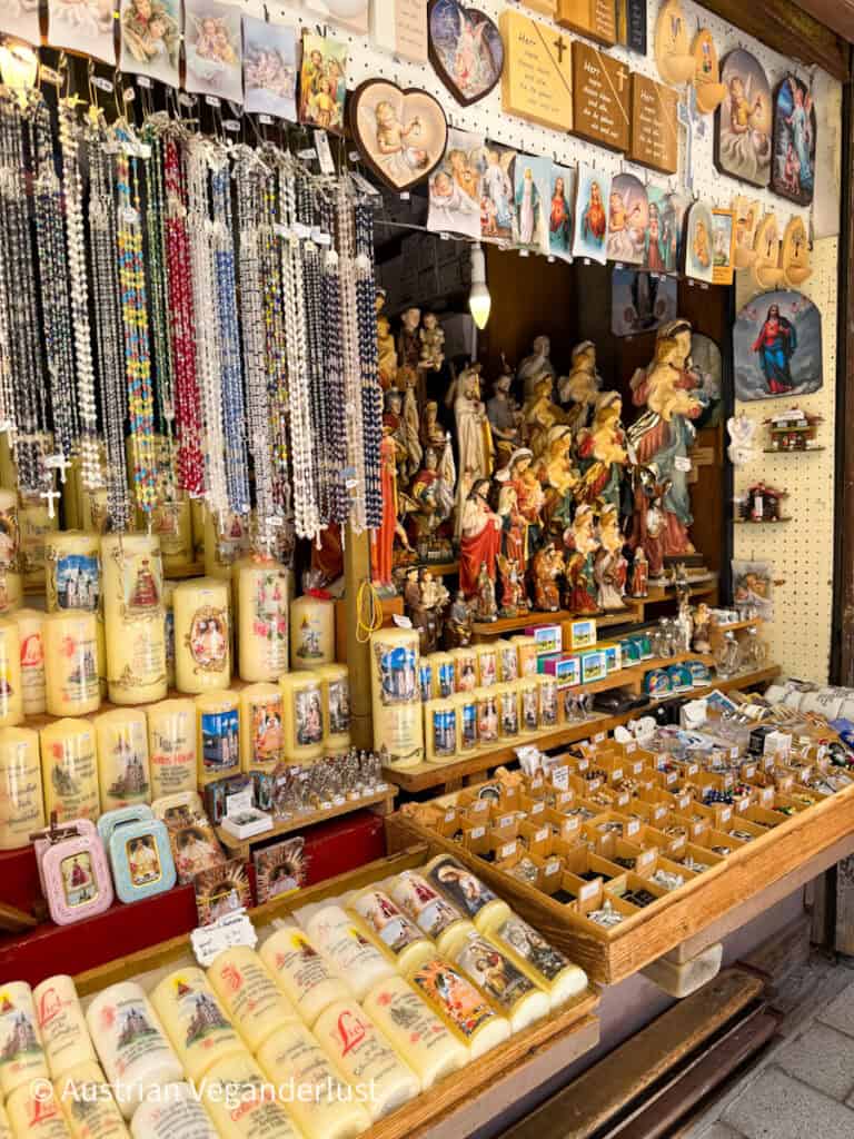 Ein belebter Souvenirstand voller religiöser Kerzen, Rosenkränze, Heiligenfiguren und Postkarten, die alle fein säuberlich in Holzschalen und an Wandhaken aufgereiht sind.