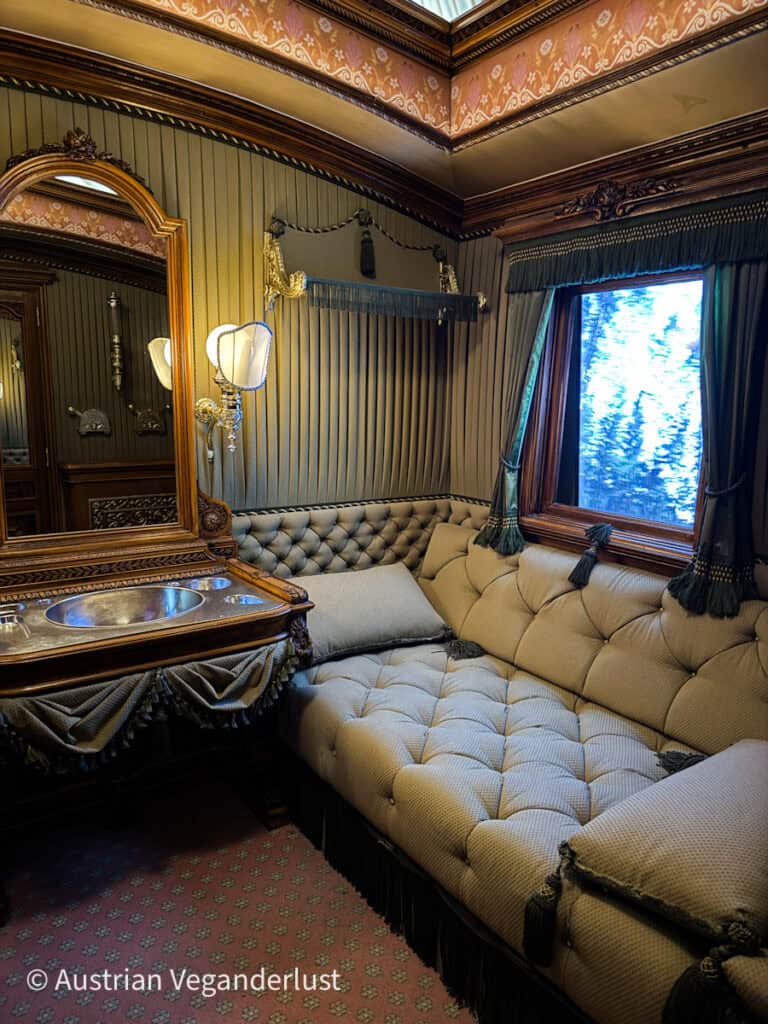 The richly decorated interior of a historic train car features tufted upholstery, tasseled curtains, and a mirrored vanity, evoking the opulence of imperial travel.