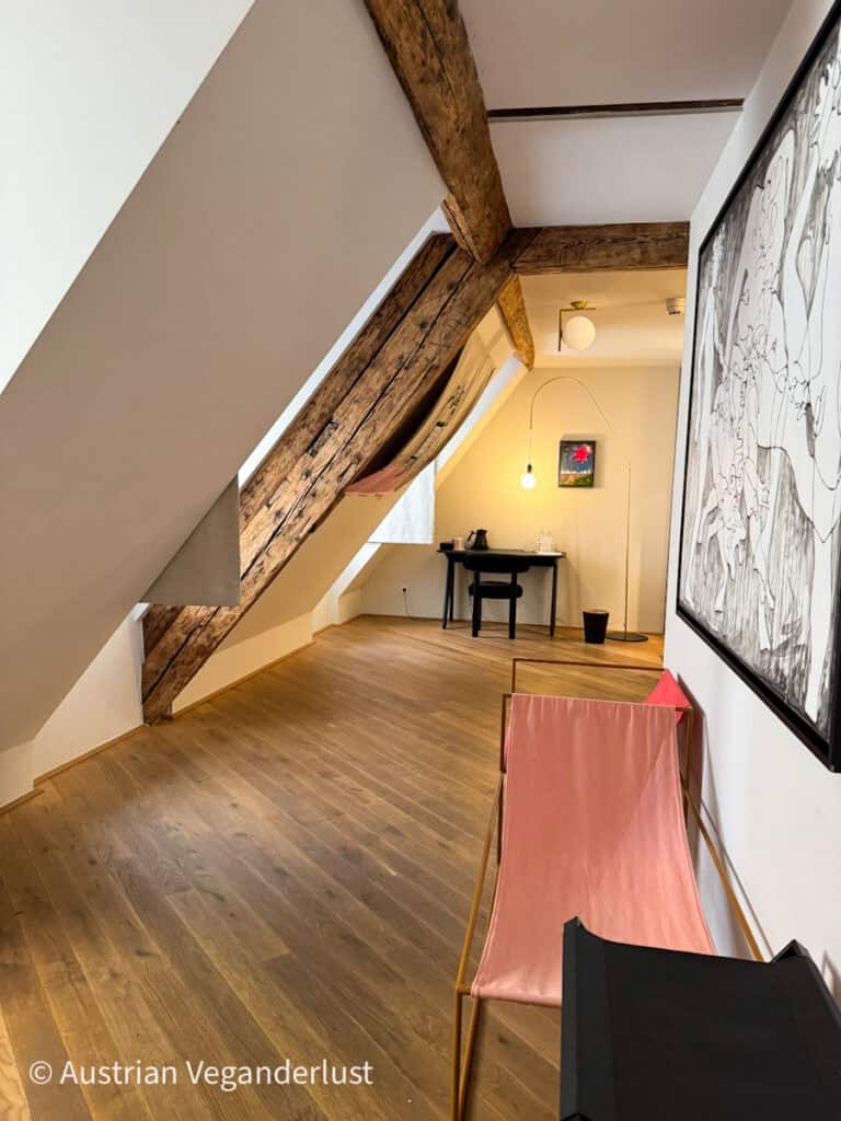 Heller und luftiger Innenflur mit freiliegenden Holzbalken, schräger Decke, moderner Kunst, einem kleinen Schreibtisch und einem rosa Sling-Stuhl in modernem Design.