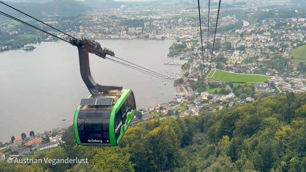 Die grüne Grünbergbahn gleitet über einen dicht bewaldeten Hang und bietet einen Panoramablick auf Gmunden, Österreich, mit seinen Gebäuden, die sich um den Traunsee gruppieren.