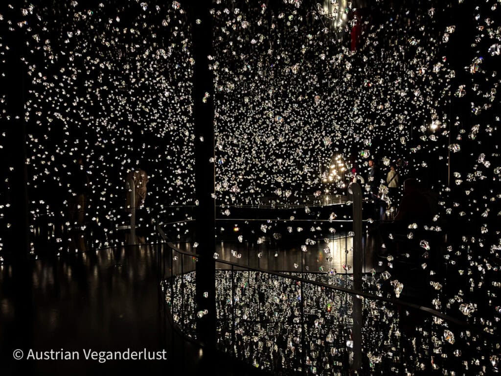 Dazzling display of countless small suspended crystals reflecting light in a darkened room, creating the illusion of floating stars or a glittering galaxy.