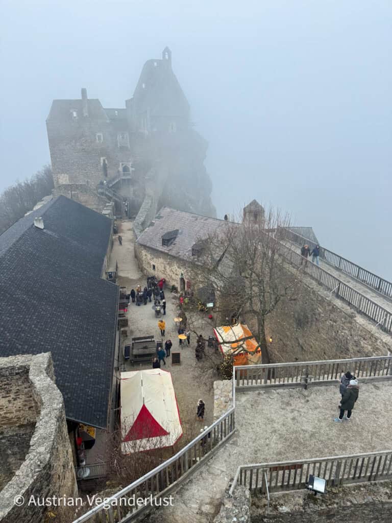Misty aerial view of Burg Aggstein’s upper levels with castle buildings and Christmas stalls nestled within the stone ruins