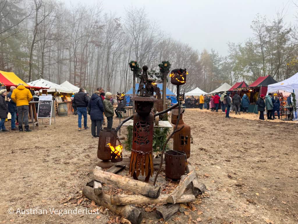 Open-air Christmas market in the woods with rustic fire pits, handmade crafts, and colourfully topped vendor tents on a foggy day