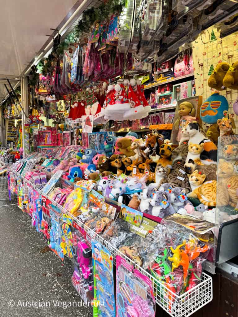 A colorful Christmas market toy stall in Linz overflowing with stuffed animals, dolls, and novelty toys, with Santa hats and holiday decor above the displays.