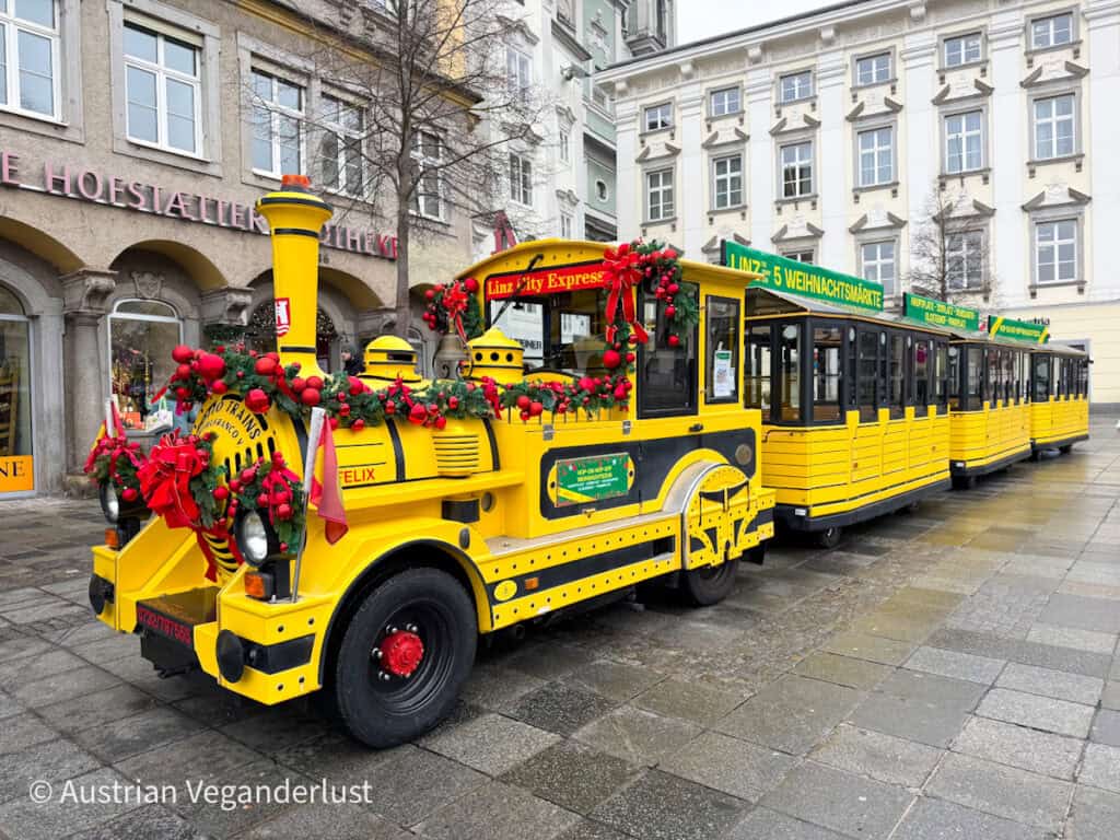 Close-up of the cheerful yellow Linz City Express train covered in red holiday decorations and greenery, offering festive rides between Linz Christmas markets.