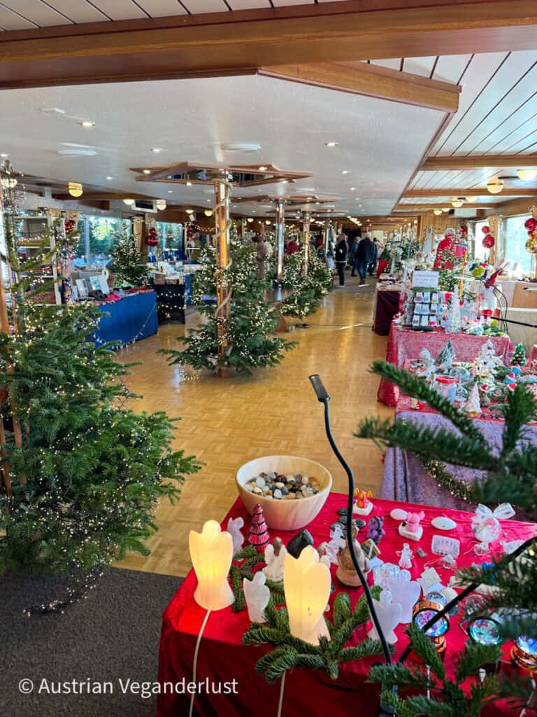 Interior of a festively decorated ship transformed into a holiday market, lined with small Christmas trees, red tablecloths, and artisan gift stalls at the Dürnstein Christmas markets.