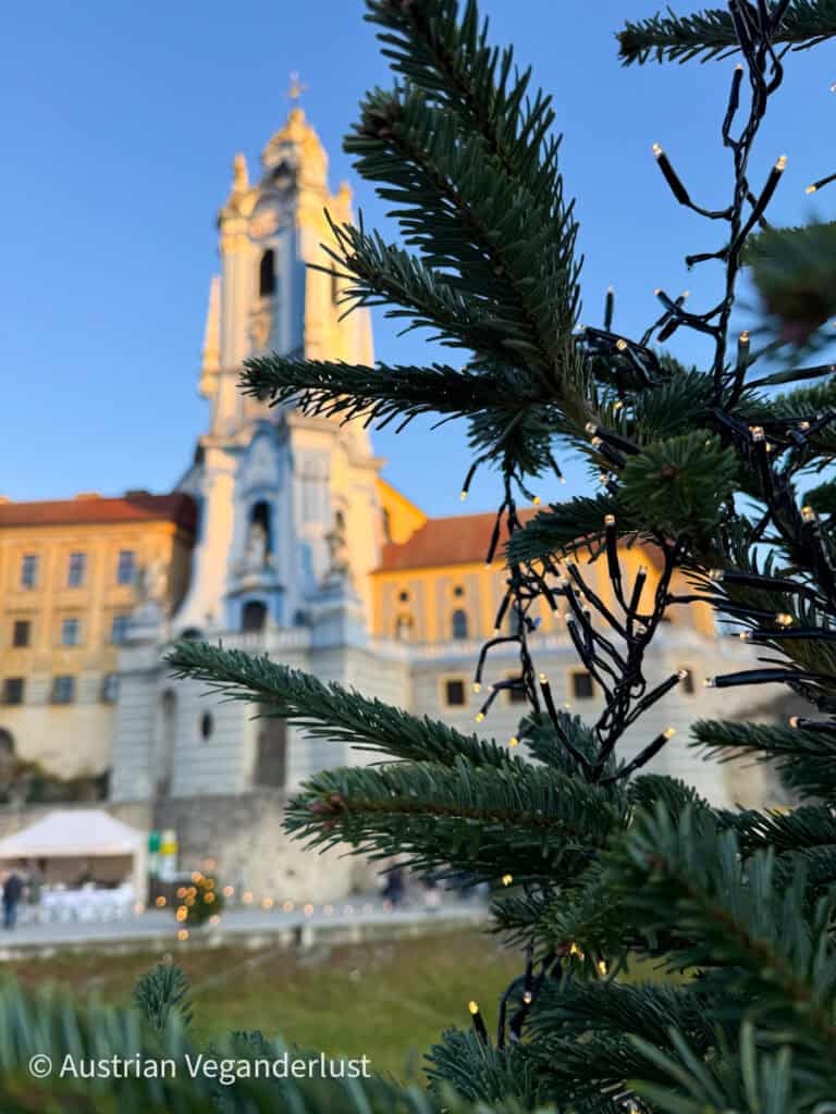 Close-up of a pine branch wrapped in Christmas lights with a softly focused view of the Dürnstein church tower in the background, capturing festive spirit in the Wachau Valley.