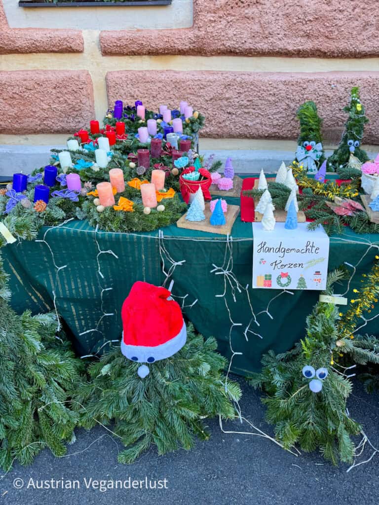 Vibrant display of handmade candles and pine decorations at an outdoor stall labeled “Handgemachte Kerzen,” part of the festive craft offerings at the Dürnstein Christmas markets.