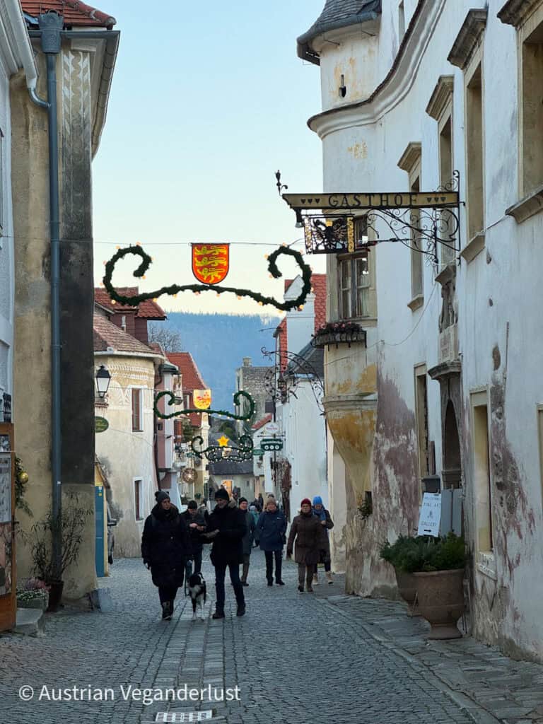 Visitors walking through a cobbled street in Dürnstein lined with medieval buildings and festive garlands, showcasing the charming village atmosphere during the Christmas markets.