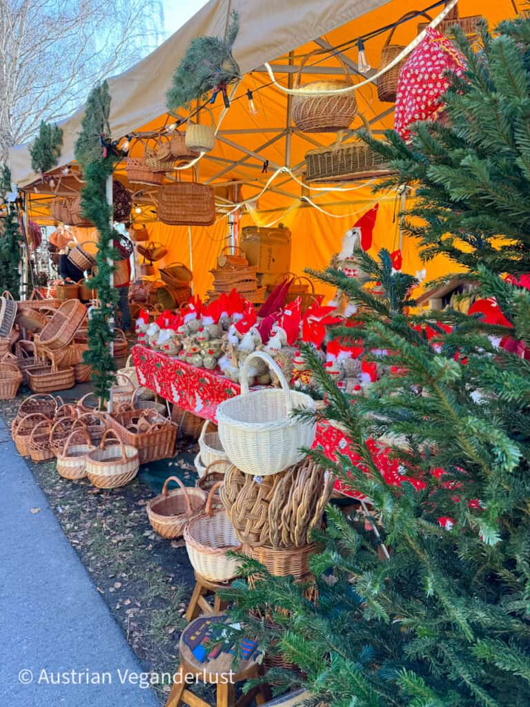Rustic market stall with handmade wicker baskets and red holiday decor, set under an orange canopy and surrounded by pine trees at the Dürnstein Christmas markets.