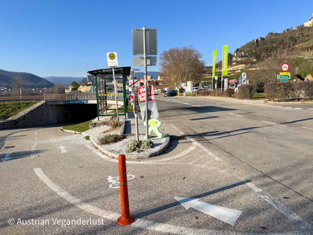 Main road leading into Dürnstein with directional signs, a bus stop, and pedestrian paths under a clear sky, helping guide visitors arriving for the Dürnstein Christmas markets.