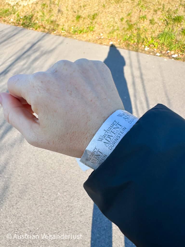 Close-up of a hand wearing a white wristband labeled “Wachauer Advent Dürnstein,” showing entry to the Dürnstein Christmas markets in the Wachau Valley under clear winter sunlight.