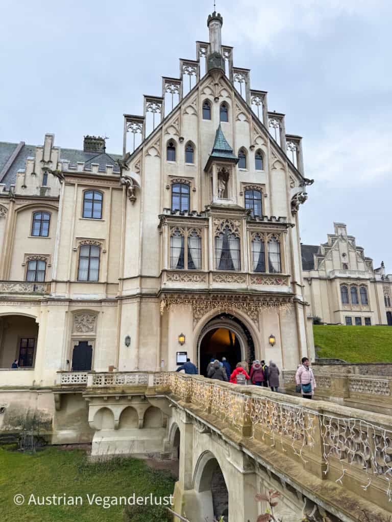 Visitors walking up the decorated stone bridge to enter Grafenegg Castle for the Christmas market on an overcast winter day.