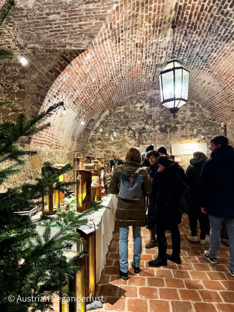 Rustic lanterns glowing warmly inside a vaulted brick cellar, where guests browse handmade decor at the Grafenegg Castle Christmas Market.