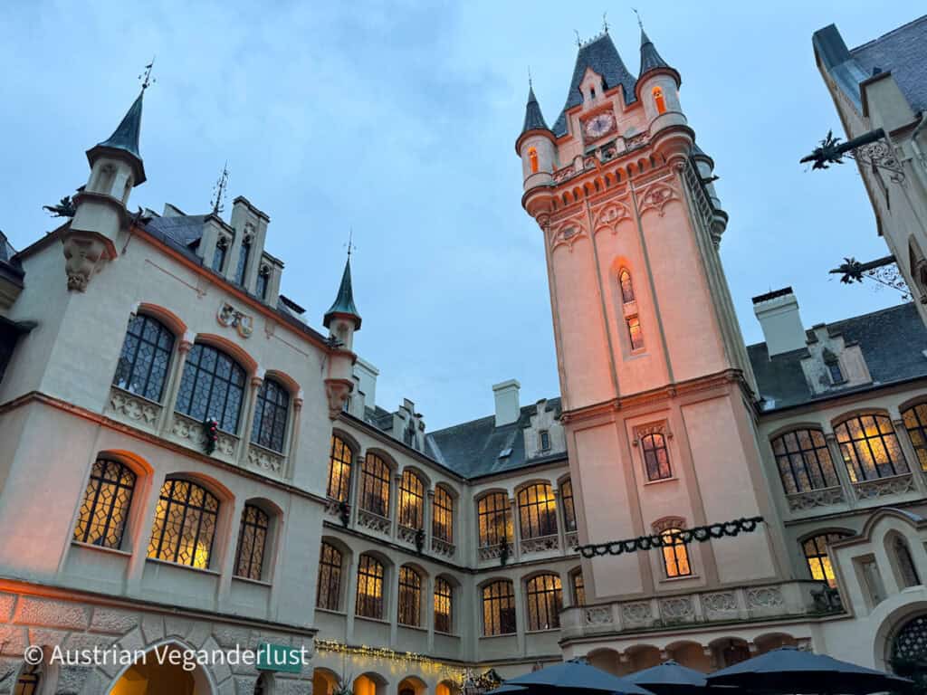 Looking up at the Gothic-style courtyard of Grafenegg Castle with arched windows and a central tower lit for the holiday season.
