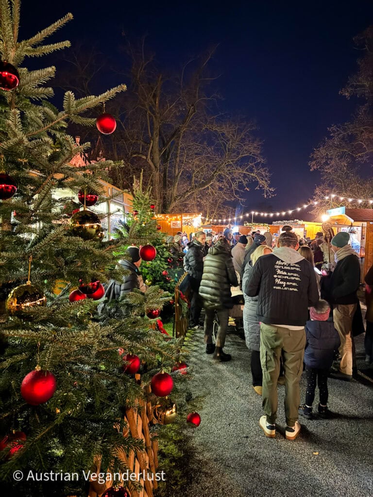 Festive fir trees decorated with red and gold baubles lining the walkway as guests explore the Grafenegg Castle Christmas Market.