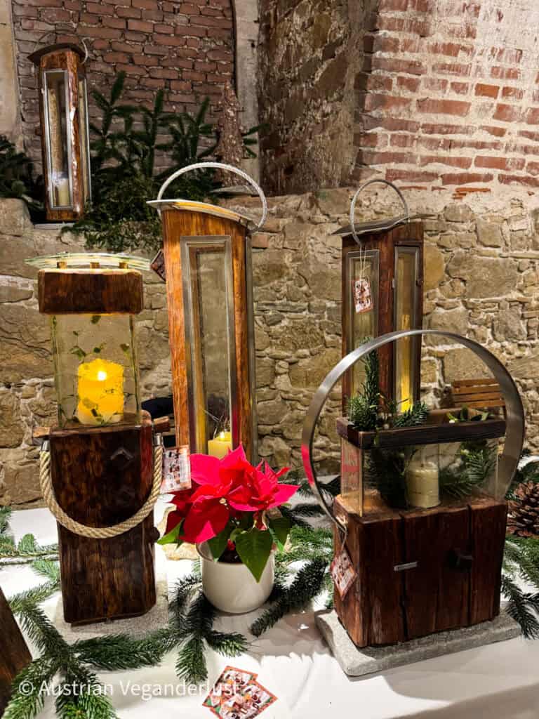 Rustic wooden lanterns and a red poinsettia displayed on a white table surrounded by pine branches at the Grafenegg Castle Christmas Market.