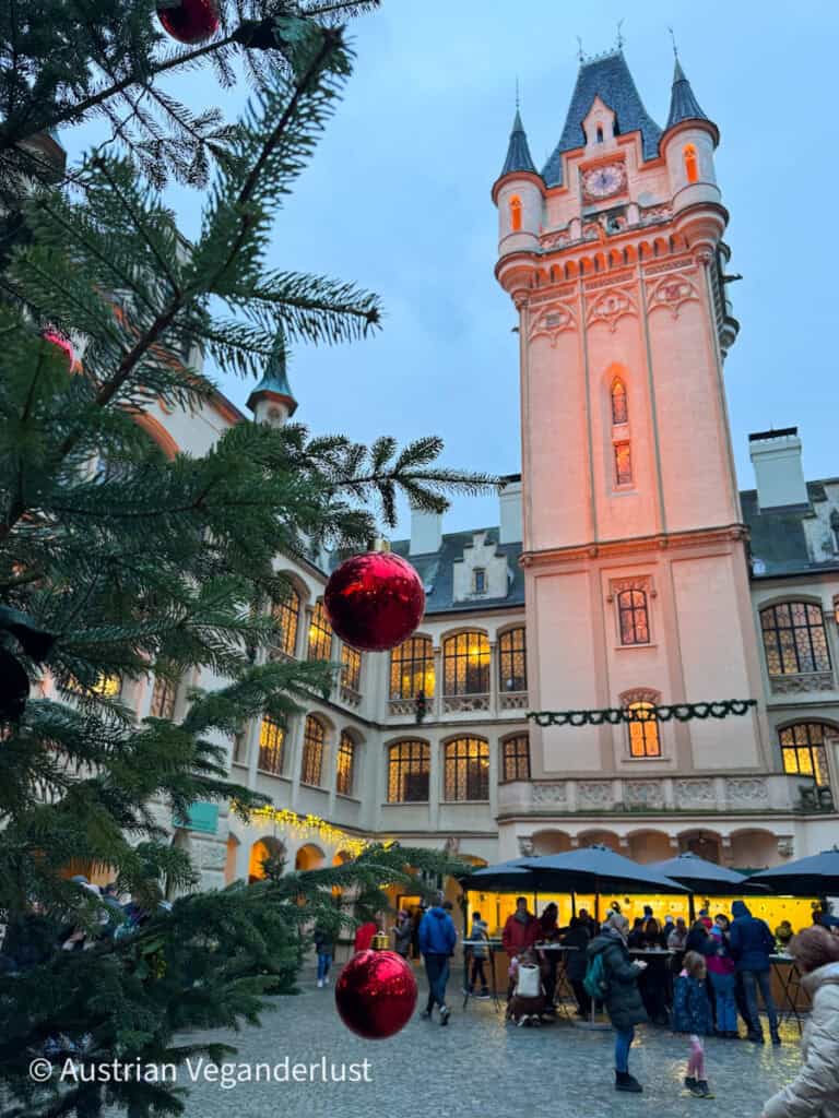 Christmas tree with red baubles in the courtyard of Grafenegg Castle, with the market atmosphere buzzing in the background.