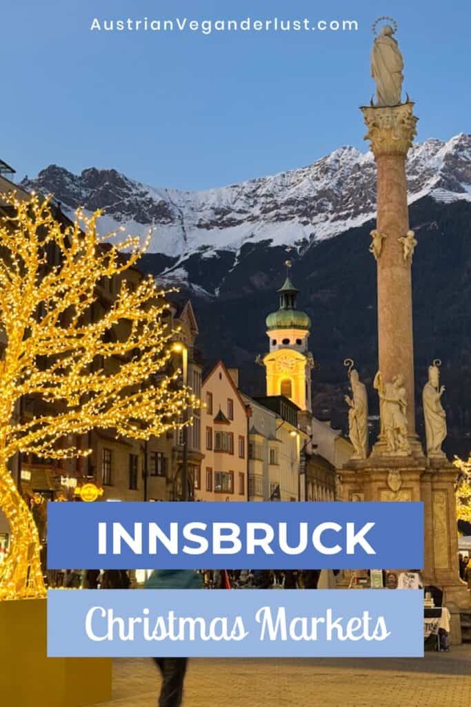 Festive street scene in Innsbruck with glowing golden light-wrapped trees, the St. Anne’s Column in the foreground, and snowy mountains in the background. Text overlay reads “INNSBRUCK Christmas Markets” with the website AustrianVeganderlust.com at the top.