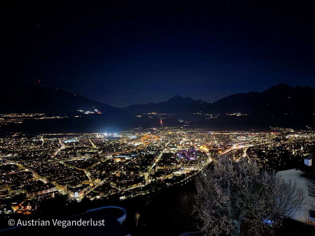 Nighttime cityscape of Innsbruck glowing with lights from above, surrounded by dark mountain silhouettes and a star-speckled sky.