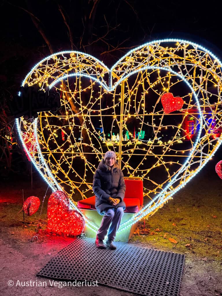 A person sits inside a giant heart-shaped light installation decorated with glowing hearts at Lumagica, creating a cozy photo spot in the illuminated park.