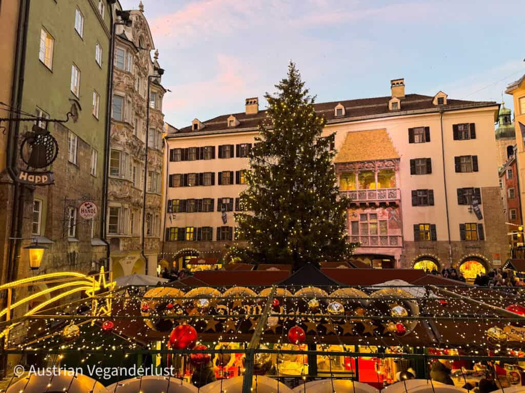 Christmas market in front of Innsbruck’s famous Golden Roof, with a large lit Christmas tree and colorful historic buildings surrounding the scene at sunset.