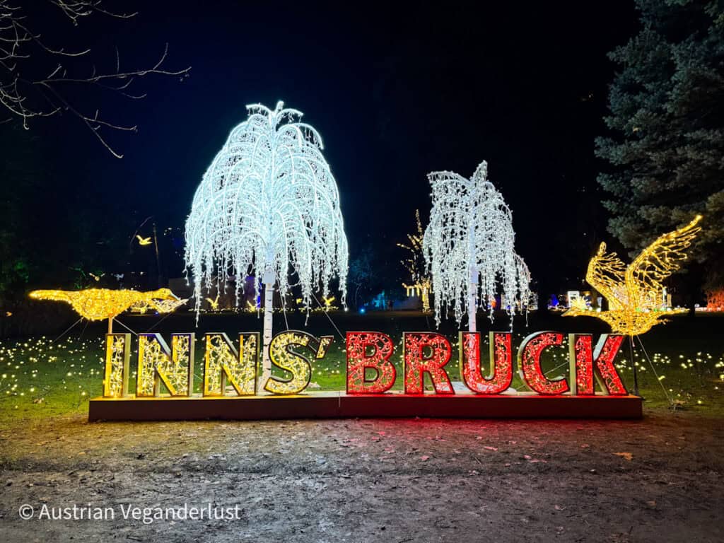 Large illuminated INNSBRUCK sign flanked by glowing willow trees and golden birds, set in a nighttime garden with festive lights.