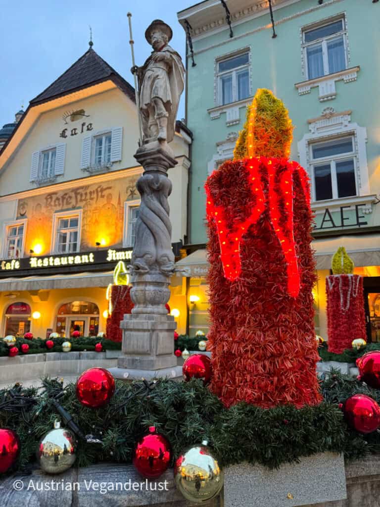 Close-up of a festive fountain display featuring giant red candles made of artificial greenery and surrounded