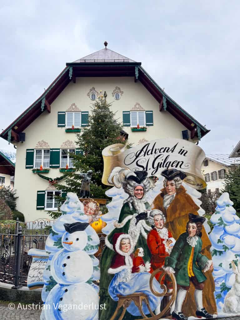Playful holiday photo board titled “Advent in St Gilgen” featuring people posing as characters in vintage winter attire, with a decorated house and tree behind.