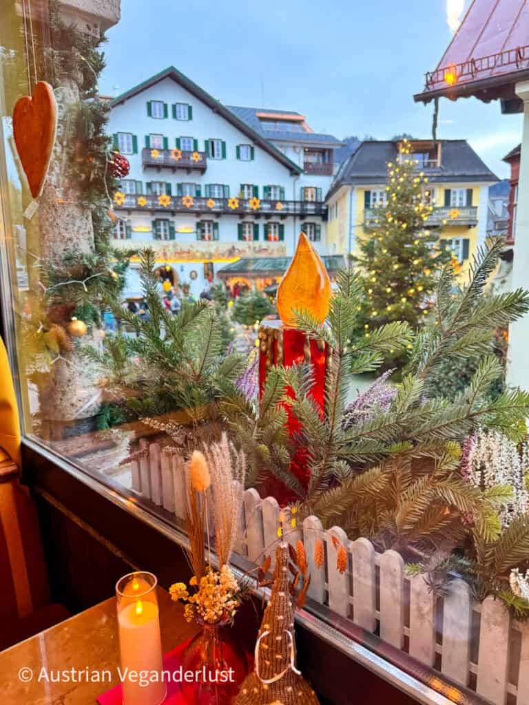 View from a cozy café window overlooking the decorated buildings and Christmas trees of St Gilgen’s market, with festive greenery and ornaments on the windowsill.