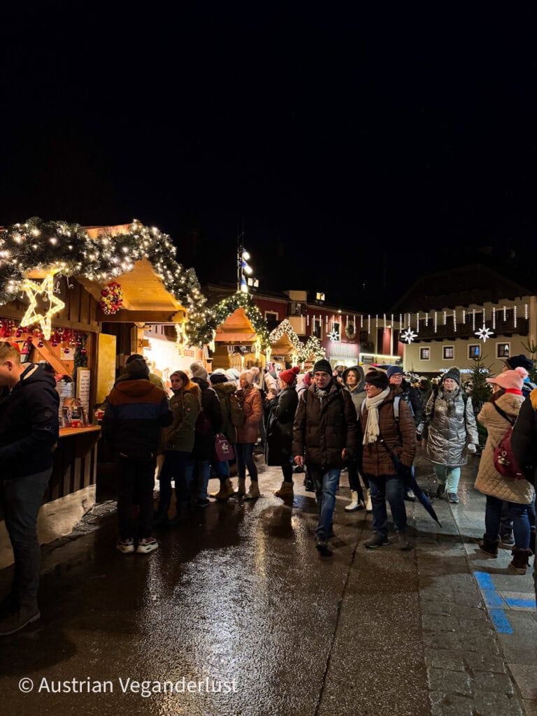 People gather around wooden huts decorated with garlands and fairy lights at night in the St. Wolfgang Christmas market.