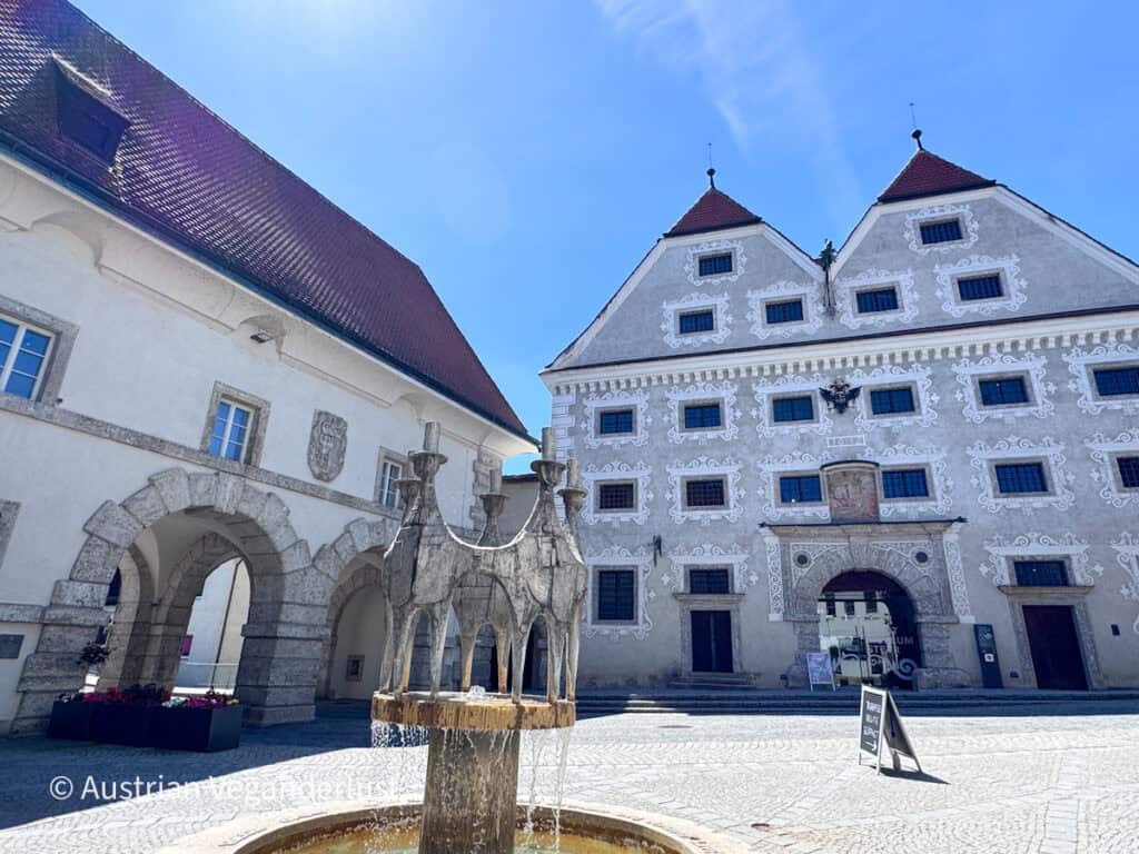 Historic courtyard with an ornate stone fountain in front of a Renaissance building decorated with white sgraffito patterns.