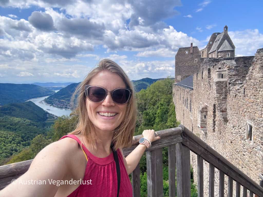 Tina standing on a wooden viewing platform at Burgruine Aggstein with the castle walls behind and the Danube Valley stretching into the distance under dramatic clouds.